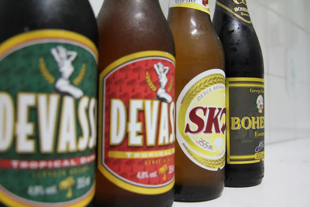 Four bottles of cerveja are lined up: two with Devassa labels, one Skol, and one Bohemia. Each showcases Brazils vibrant beer culture with distinct tropical-themed branding, offering an enticing introduction to beer in Brazil.