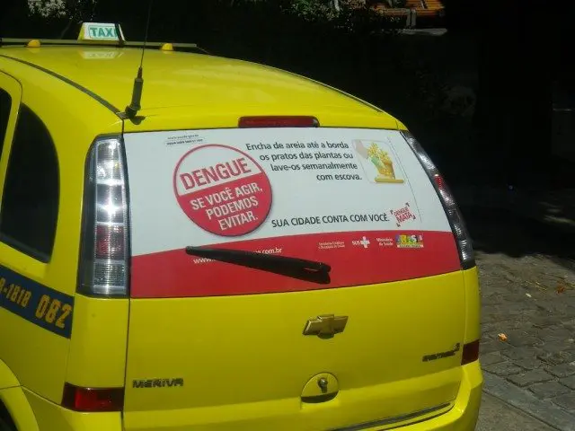 A yellow taxi with a sign on the back, parked during a dengue fever outbreak.