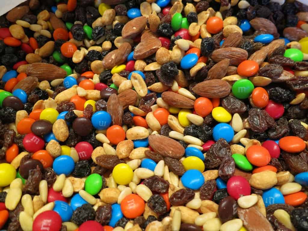 A close-up of trail mix showcases colorful candy-coated chocolates, almonds, peanuts, raisins, and pine nuts. This delightful assortment highlights a vibrant array of colors and textures.