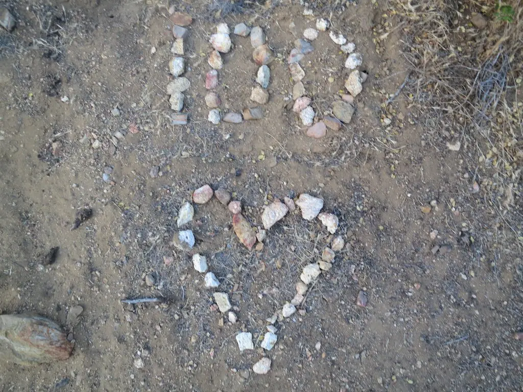Stones are arranged on the ground to form the number 100 above a heart shape, marking the first 100 PCT miles. Dry grass and soil surround the design, reflecting lessons learned along this iconic trail.