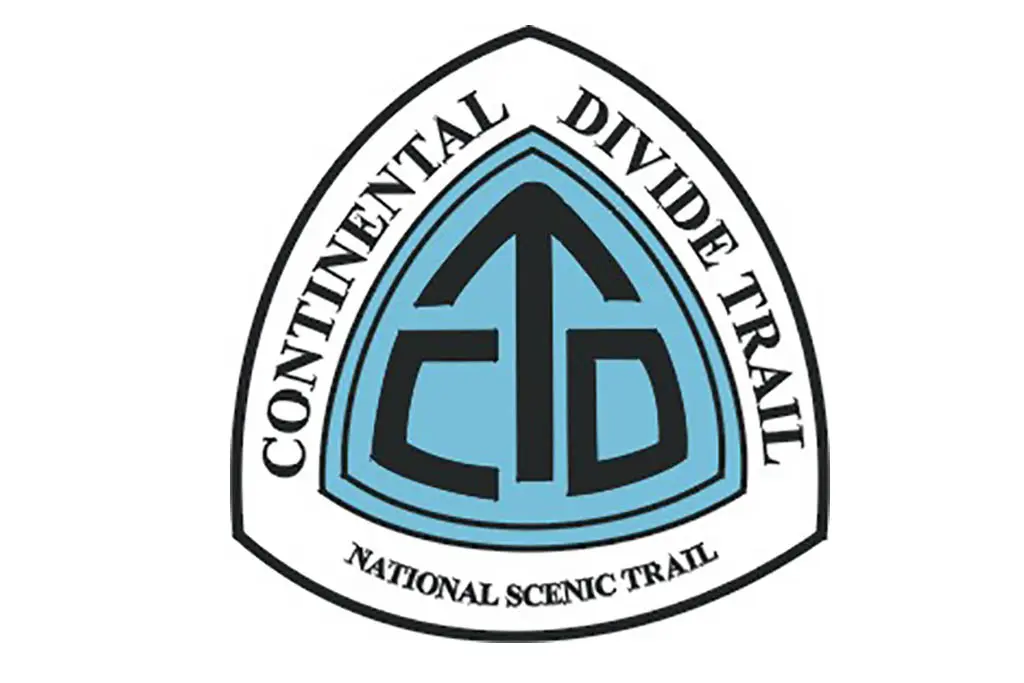 The logo of the Continental Divide Trail showcases a white triangle with a black outline. Within, a blue backdrop features a stylized black arrow accompanied by the initials CDT. The text elegantly states Continental Divide Trail National Scenic Trail.