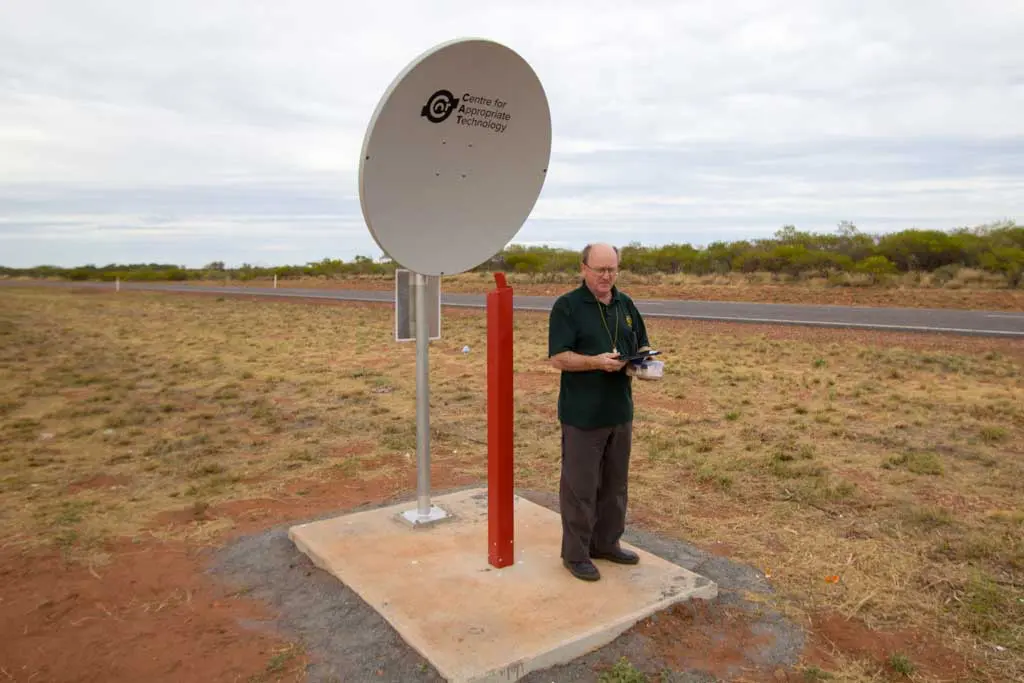 A person stands next to a weather monitoring device mounted on a metal pole in a dry, grassy field near a road. Branded with the Centre for Appropriate Technology logo, it serves as a waypoint on the Australia Bike Tour, documenting conditions since Day 45.