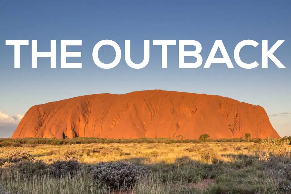 Uluru, a majestic rock formation, glows orange against a clear blue sky, embraced by the grassy plains of the Outback. Bold white letters spell THE OUTBACK across the top.