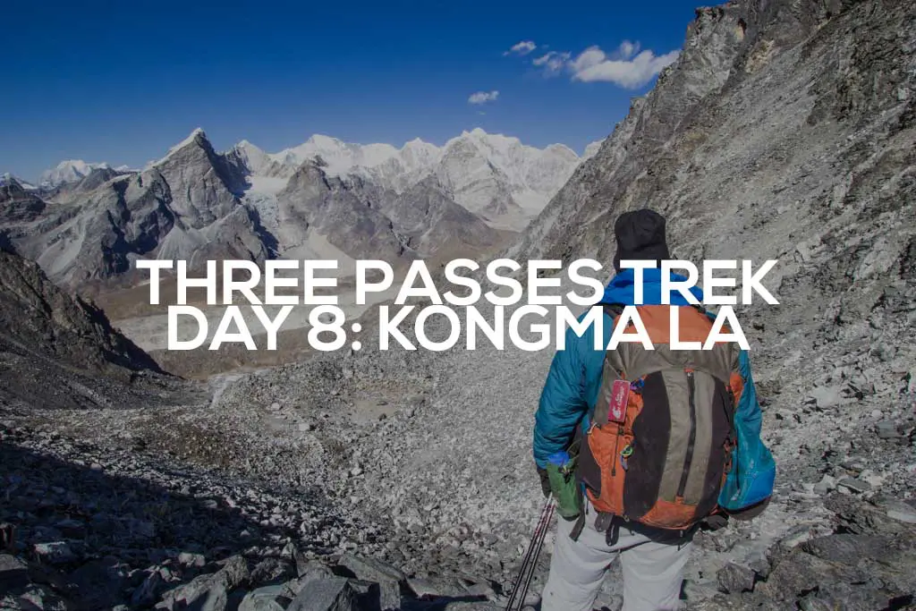 A trekker with a backpack stands on a rocky trail, overlooking the majestic Kongma La under a blue sky. Text overlay reads: Three Passes Trek Day 8: Kongma La. Snow-capped peaks shine brilliantly in the distance.