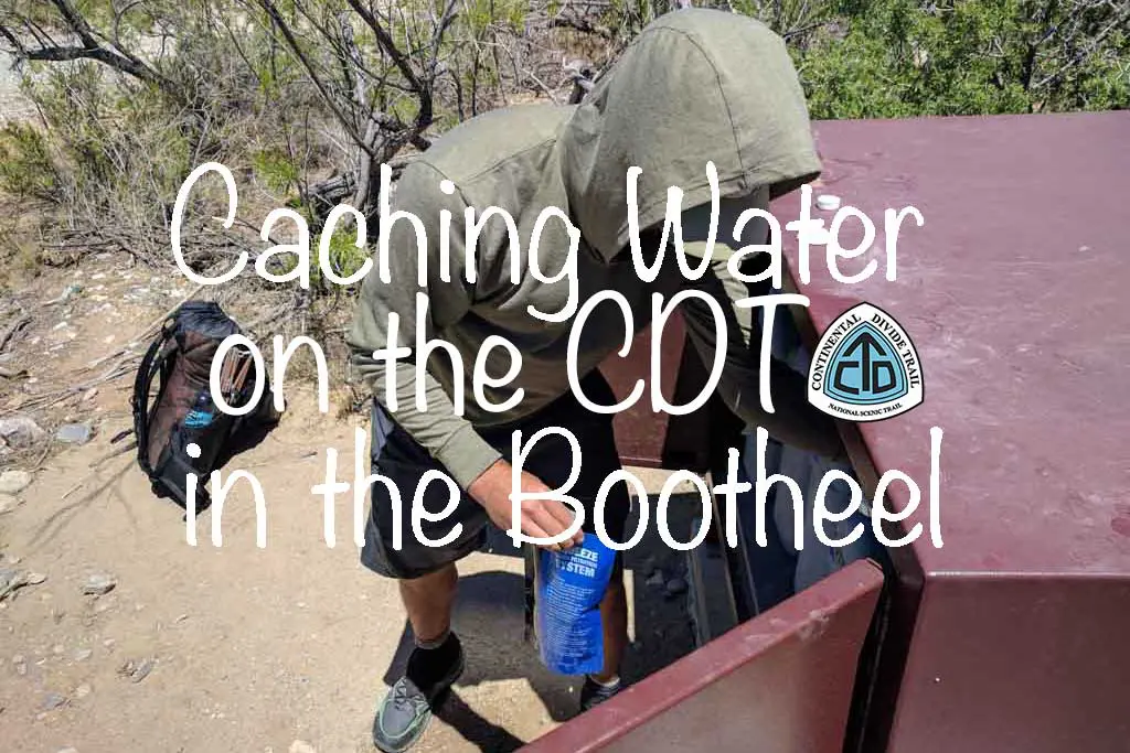 A person in a green hoodie is caching water from a container on the back of a red vehicle along the CDT in New Mexicos Bootheel. A backpack rests on the ground nearby, capturing the essence of adventure.