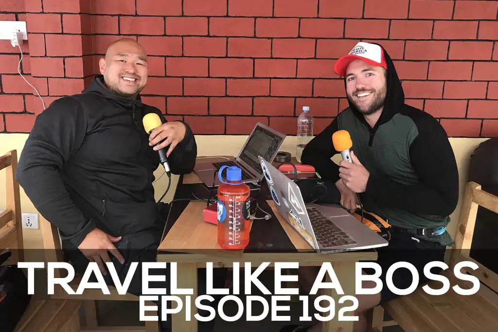 Two men sit at a table with microphones, recording equipment, and laptops, smiling towards the camera. The text Travel Like A Boss Episode 192 appears at the bottom, set against a backdrop of a rustic brick wall.