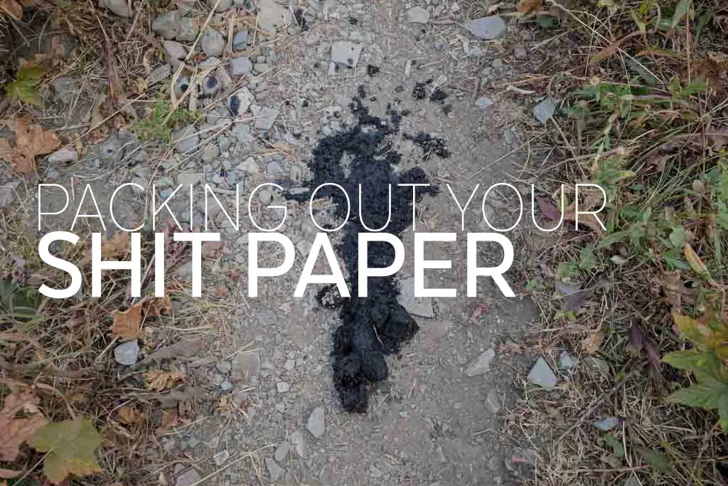 A dirt path, lightly dusted with dark matter, winds through grass and small rocks. The phrase PACKING OUT YOUR SHIT PAPER is boldly overlaid, reminding hikers of their responsibility to carry out toilet paper.