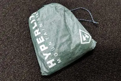 A green drawstring bag from Hyperlite Mountain Gear, perfect for storing your essentials or even a ground cloth, rests on a dark textured surface. The bag proudly displays its logo and brand name in crisp white lettering.