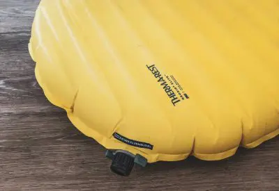 Yellow camping air mattress featuring a black valve, clearly labeled as Therm-a-Rest NeoAir XLite, rests on a wooden surface. The label proudly indicates its Regular size, perfect for outdoor adventures.