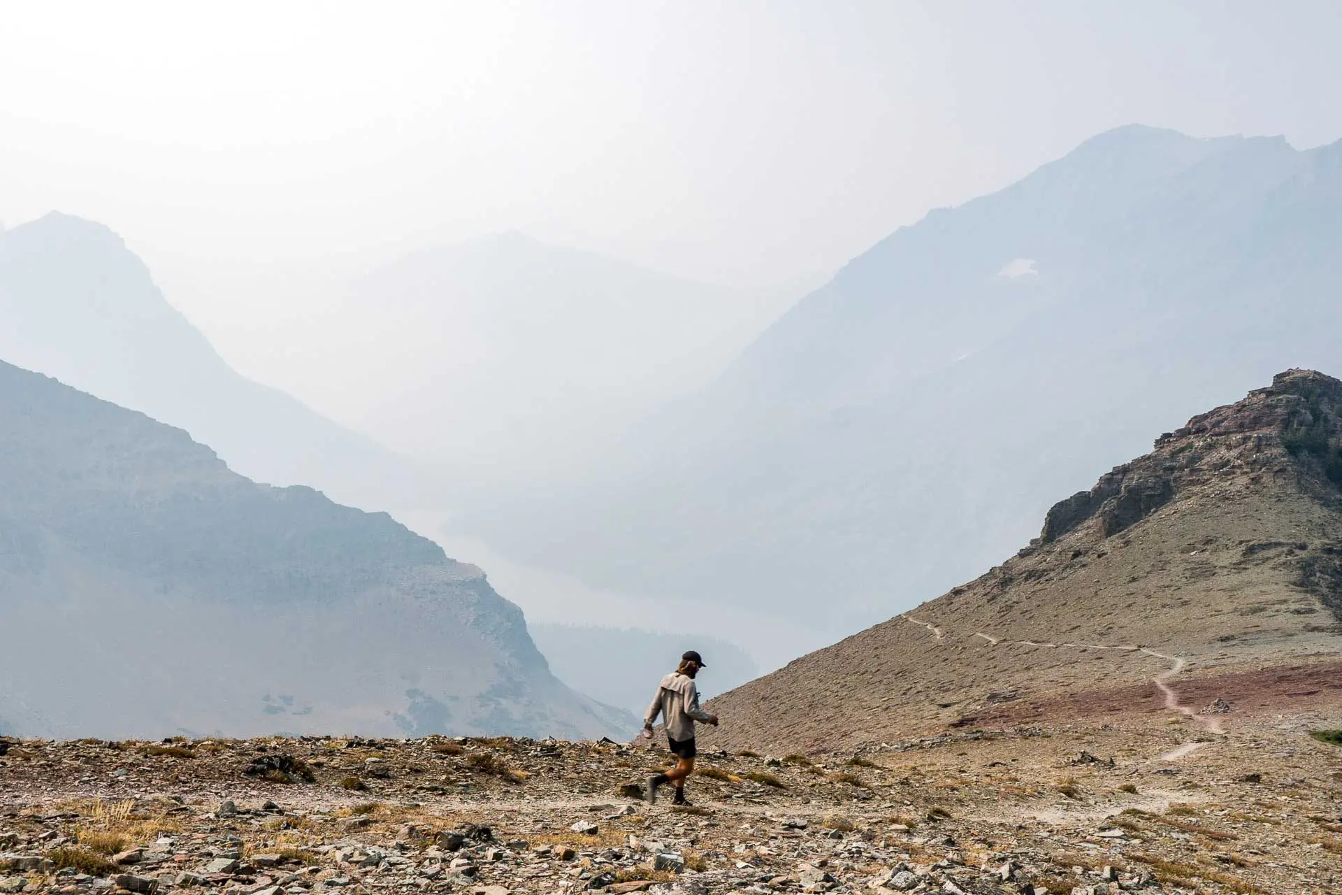 A solitary figure navigates the rocky mountain path, with hazy, towering peaks looming in the background under an overcast sky. The scene echoes a setting straight out of CDT horror stories.