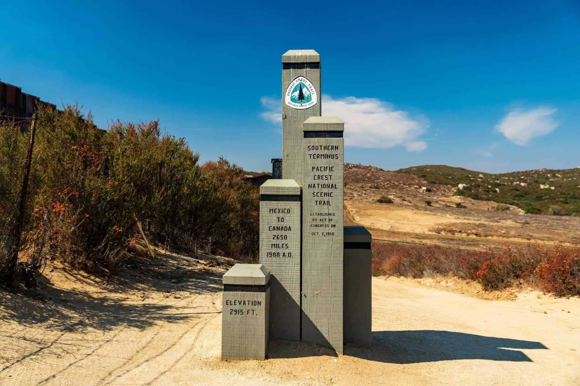 Monument near the southern terminus of the Pacific Crest National Scenic Trail, as noted in the 2021 Pacific Crest Trail survey, listing the distance to Canada as 2,650 miles. Surrounded by desert landscape, bushes, and a clear blue sky.
