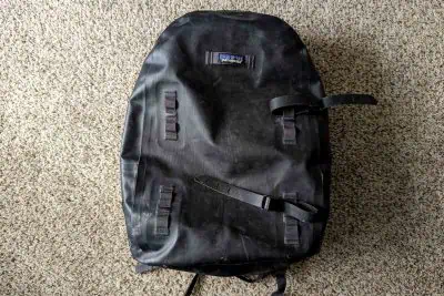 A sleek black backpack rests on the textured carpet, showcasing its Patagonia Guidewater design. The bag features a visible logo near the top, adjustable straps, and convenient loops for attachments.