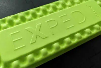 Close-up of a green EXPED FlexMat with a wavy texture, embossed boldly with EXPED. The dark background highlights its unique design.