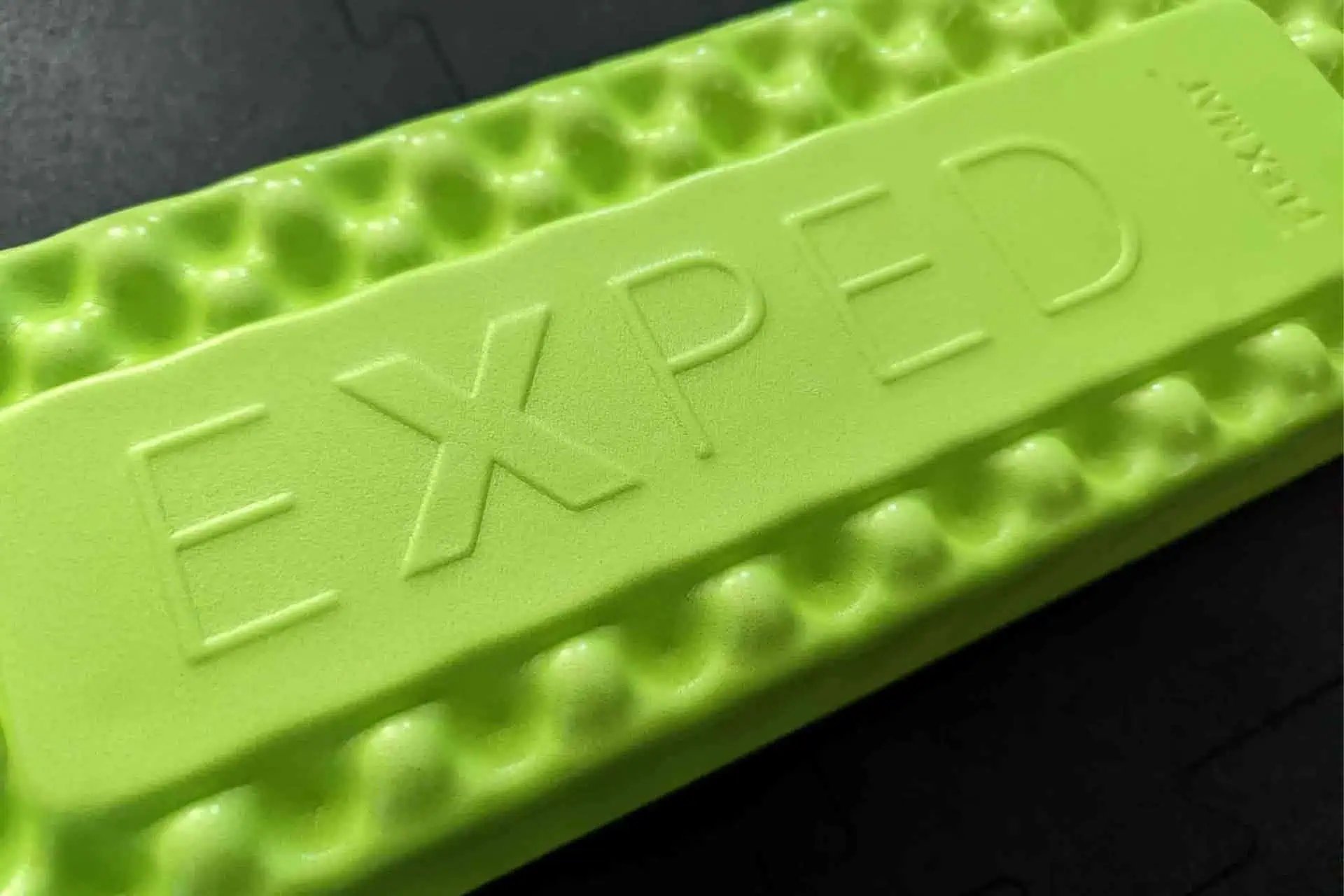 Close-up of a green EXPED FlexMat with a wavy texture, embossed boldly with EXPED. The dark background highlights its unique design.
