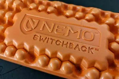 A close-up reveals the orange textured foam of the NEMO SWITCHBACK sleeping pad, where embossed text graces its center. The surface, designed for optimal comfort, features a pattern of raised, bump-like shapes for superior cushioning during your adventures.