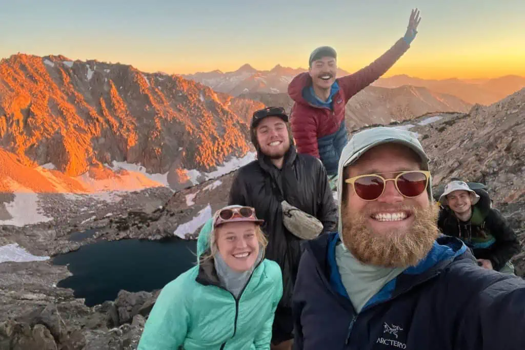 A group of smiling hikers at the top of a pass at sunset.