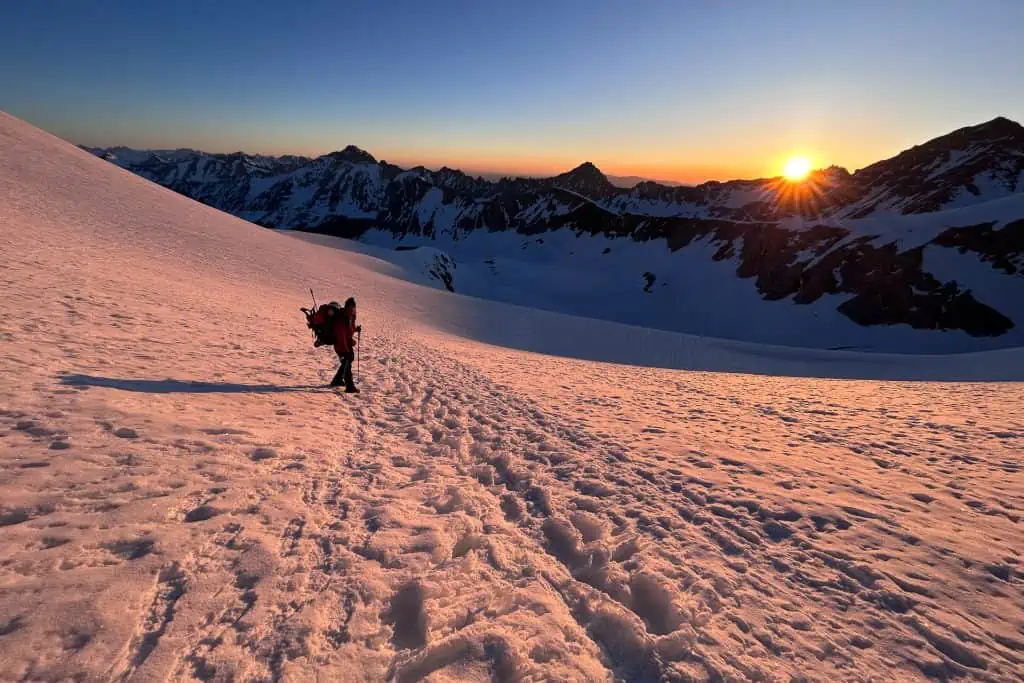 A hiker standing in a snowfield at sunset.
