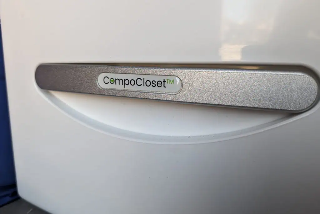 A close-up of a white surface with a metallic handle featuring the label CompoCloset™ in the center. The sleek and modern design is reminiscent of top cuddy composting toilet innovations.