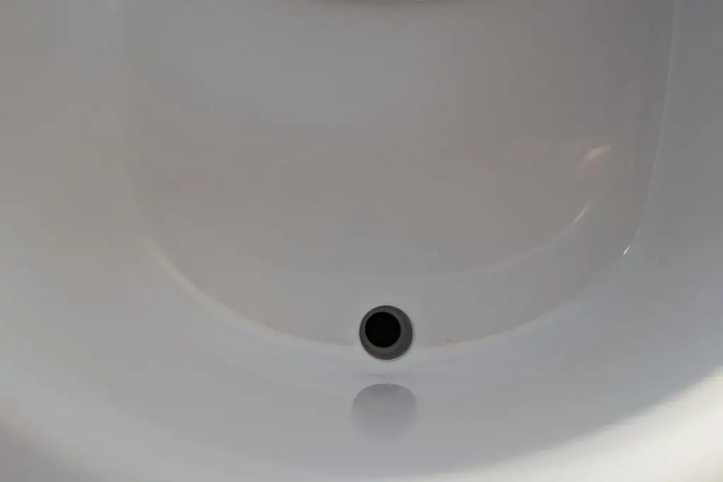 Close-up of a white ceramic sink basin with a visible drain hole near the bottom edge, reminiscent of those in cuddy composting toilet reviews. The surface is smooth and glossy, reflecting light, with a gentle curve forming the basins shape.