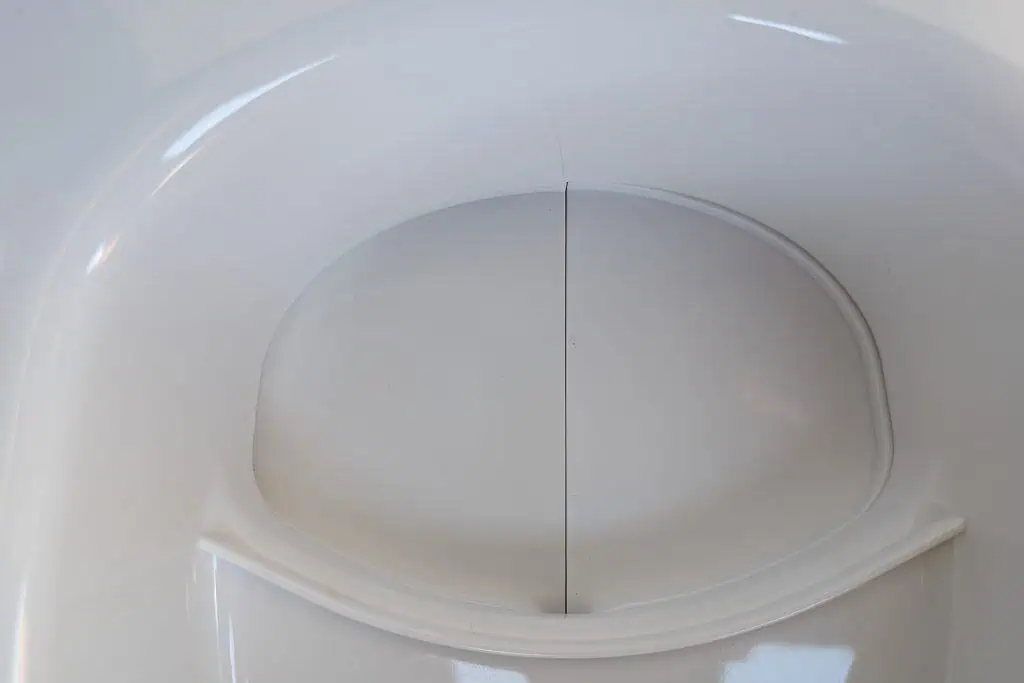 Close-up view of a white toilet seat with the lid partially open, revealing a clean, smooth surface. The lighting highlights the glossy finish and shadows accentuate its curved design—a sleek addition you might find in a top cuddy composting toilet review.