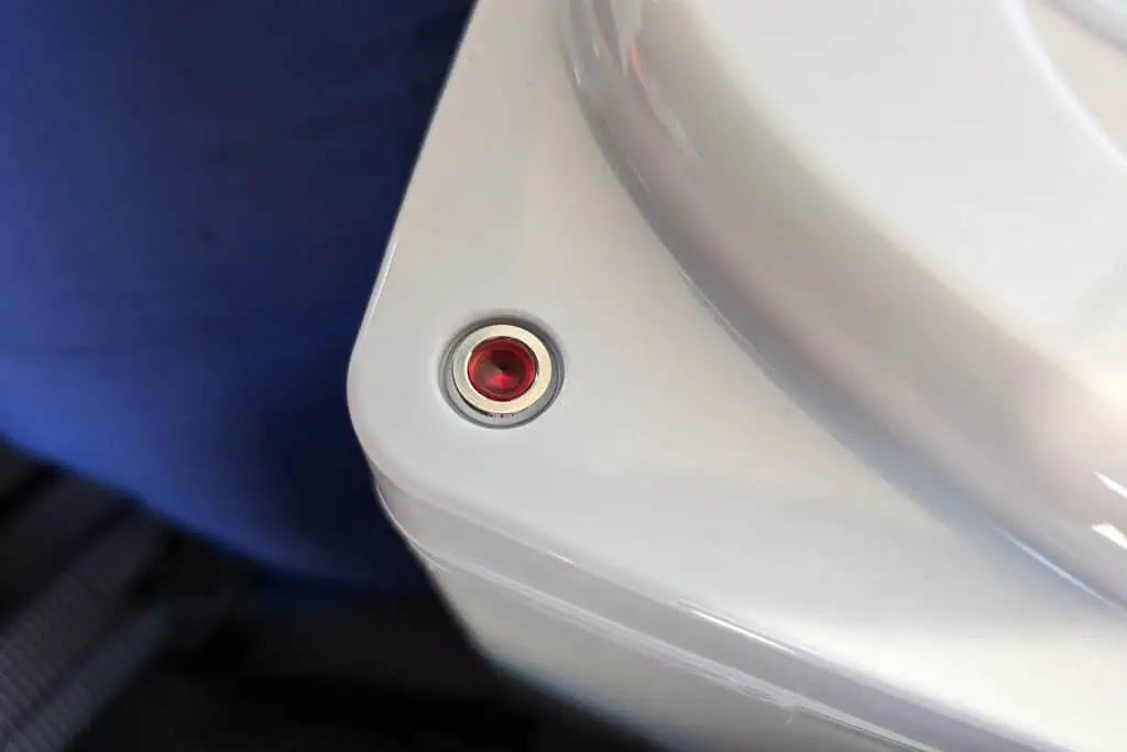 Close-up of a small red button or indicator light embedded in a sleek, white surface. A hint of blue fabric adds to the ambiance, reminiscent of the thoughtful design youd find in a top-rated cuddy composting toilet review.
