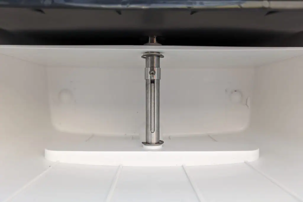Close-up view of a stainless steel rod or pin inside a white, rectangular compartment—reminiscent of the sleek design featured in many cuddy composting toilet reviews. The compartment has smooth walls and a flat base, with the rod positioned vertically in the center.