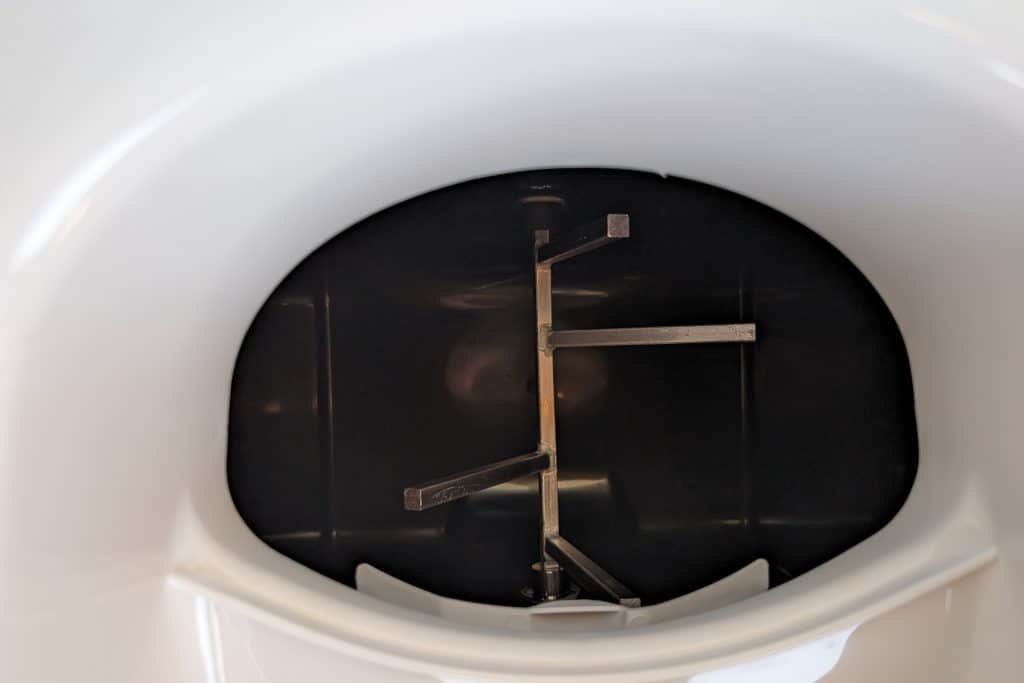 Close-up of a black and white device with metal prongs inside a rounded, white housing. The prongs are arranged in a cross pattern. The smooth and glossy design reflects its efficient engineering—a feature praised often in Cuddy composting toilet reviews.