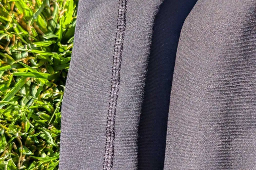 Close-up of a pair of dark gray Mammut Aenergy TR 2 in 1 Shorts with visible stitching detail on a grassy surface. The bright green, freshly cut grass enhances the contrast, highlighting the rich texture of both materials.