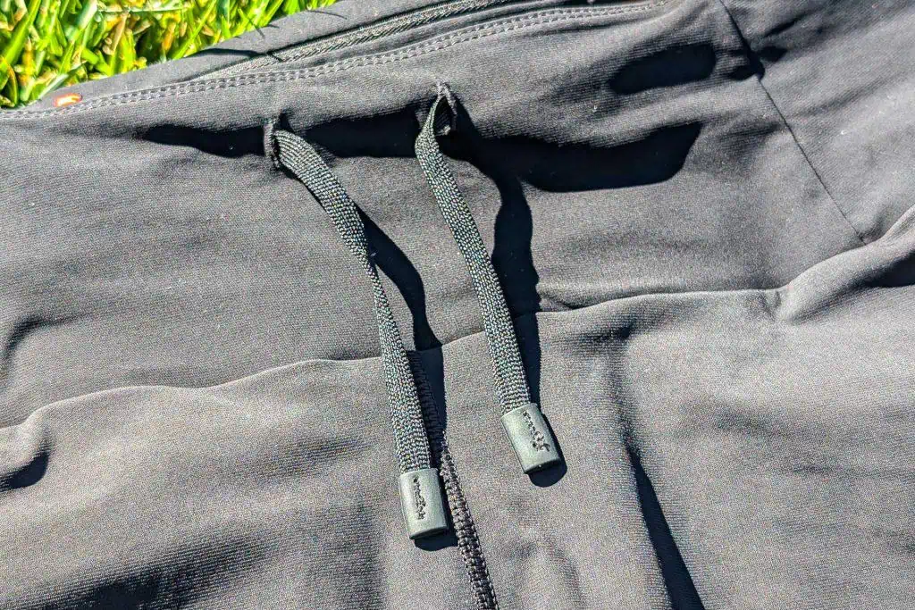 Close-up of black sweatpants with a drawstring on a grassy surface, reminiscent of Mammut Aenergy TR 2 in 1 Shorts. The drawstring features metal tips and is neatly tied, while bright lighting highlights the fabrics texture.