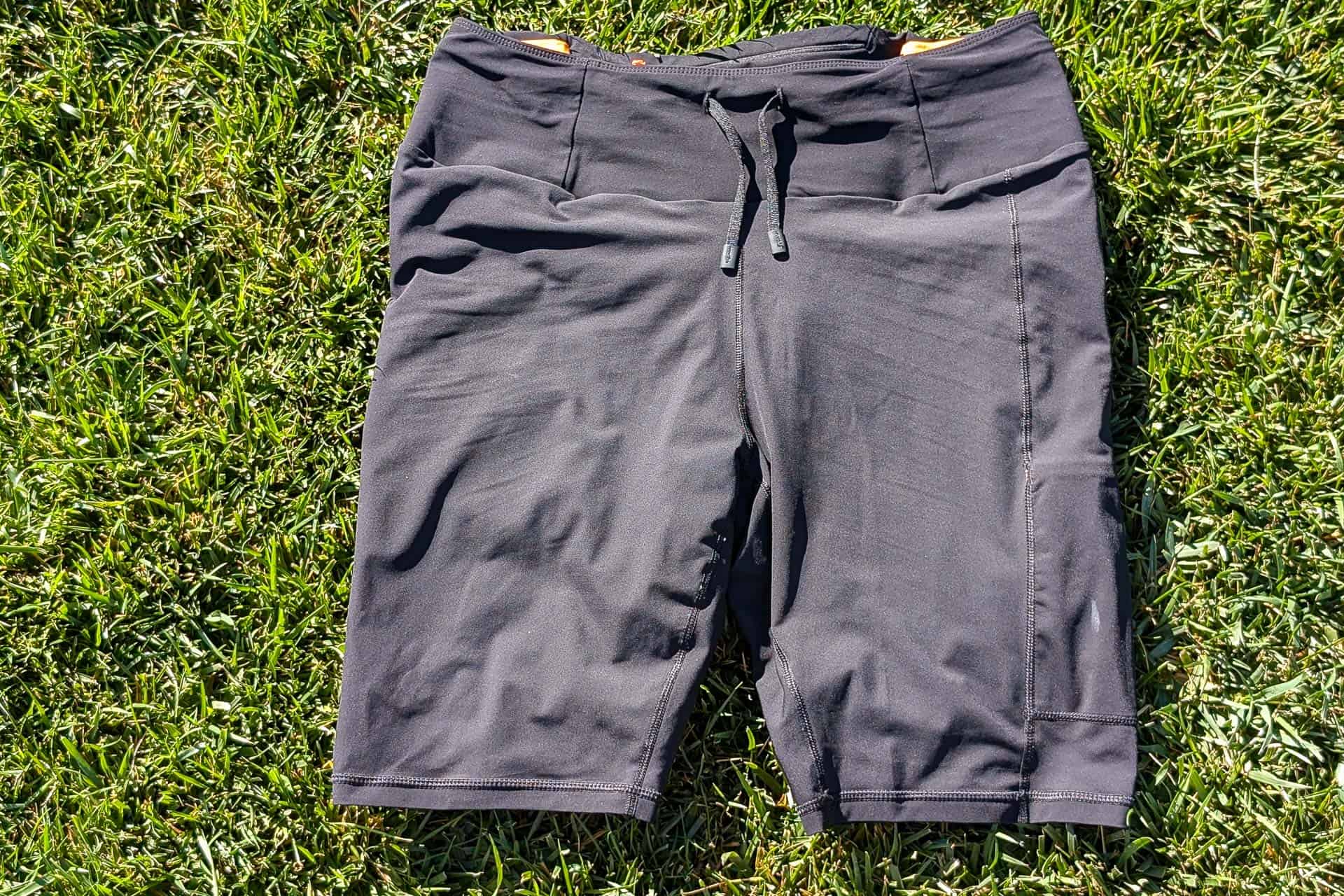 The Mammut Aenergy TR 2 in 1 Shorts rest on the green grass, their drawstring waist catching the bright sunlight.