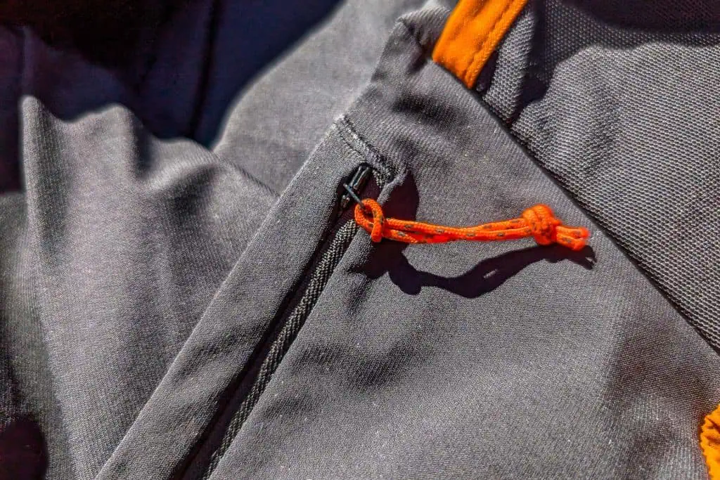 Close-up of a black fabric jacket with an orange drawstring loop attached to a zipper, much like the contrasting details found in Mammut Aenergy TR 2 in 1 Shorts. Bright lighting highlights the texture of the fabric, adding depth and interest to the garments design.