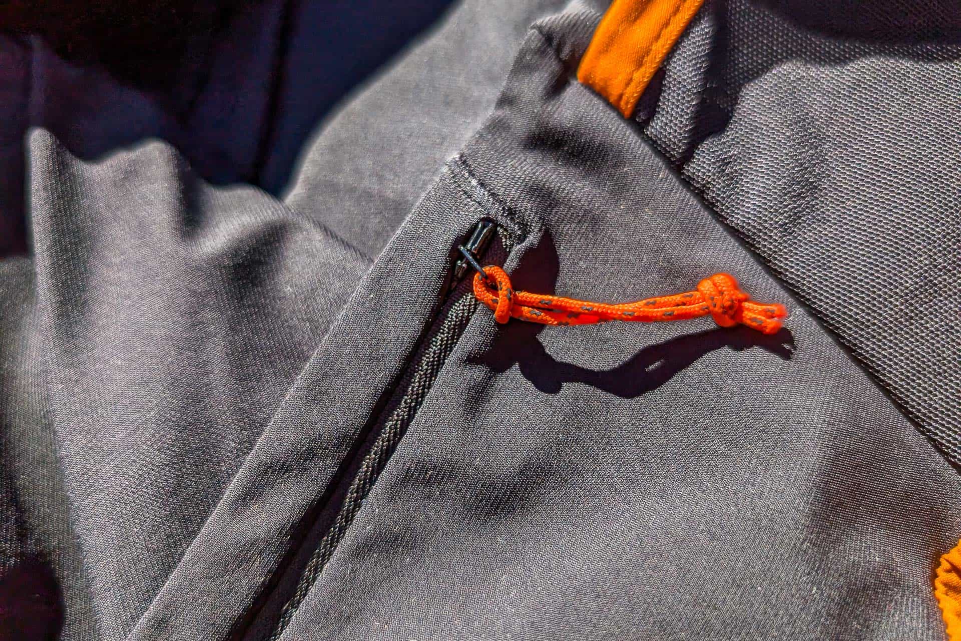 Close-up of a black fabric jacket with an orange drawstring loop attached to a zipper, much like the contrasting details found in Mammut Aenergy TR 2 in 1 Shorts. Bright lighting highlights the texture of the fabric, adding depth and interest to the garments design.