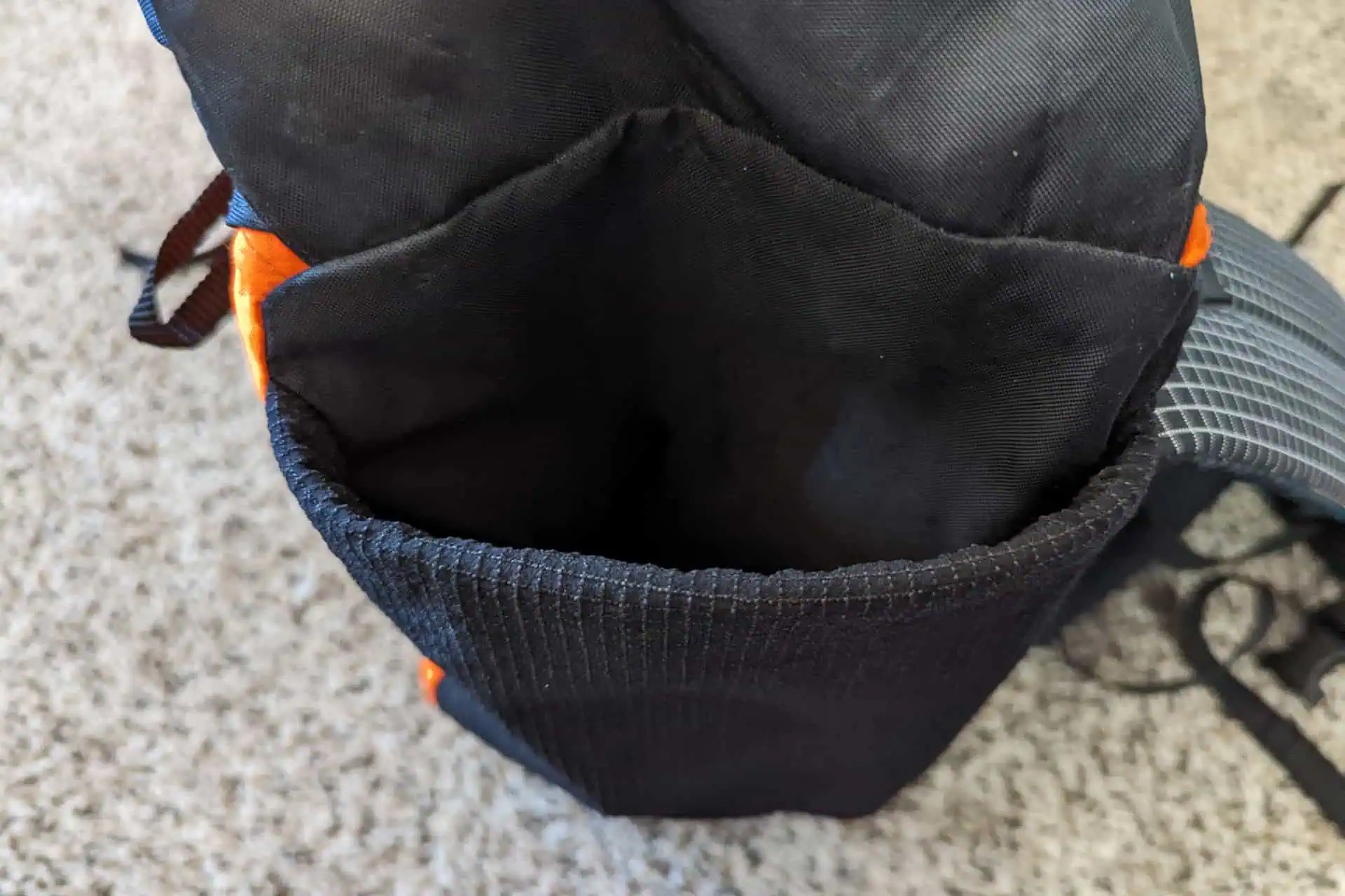An open Atom Packs Pulse backpack in striking black and orange lies on the carpeted floor, revealing its spacious main compartment. The sturdy straps are visible on the side, ready for your next adventure.