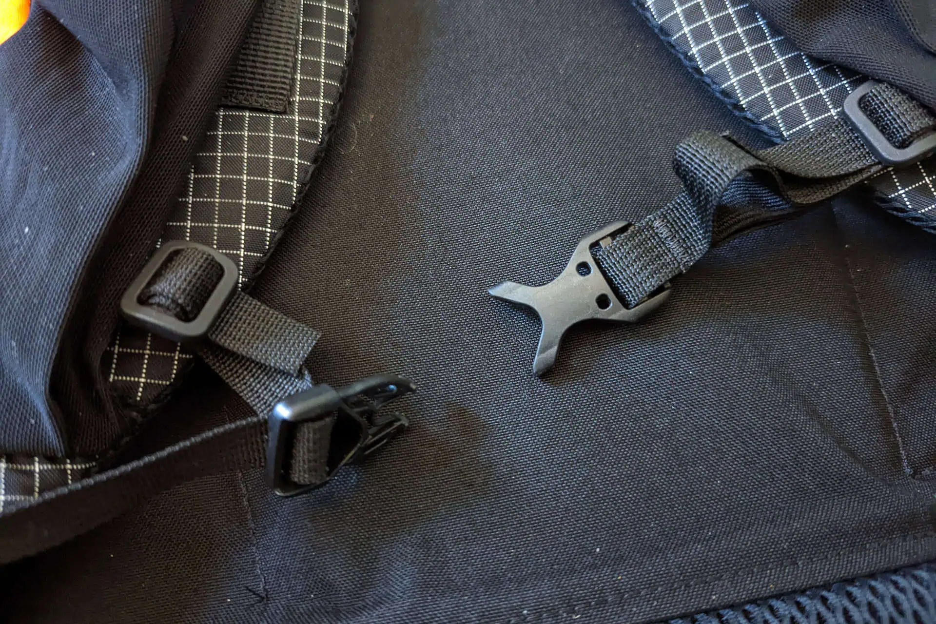 Close-up of a black Atom Packs Pulse backpack with adjustable straps and buckles. A small, grid-patterned section adorns one strap, adding texture. The smooth surface is well-lit, highlighting the intricate details of this backpacks fastenings.