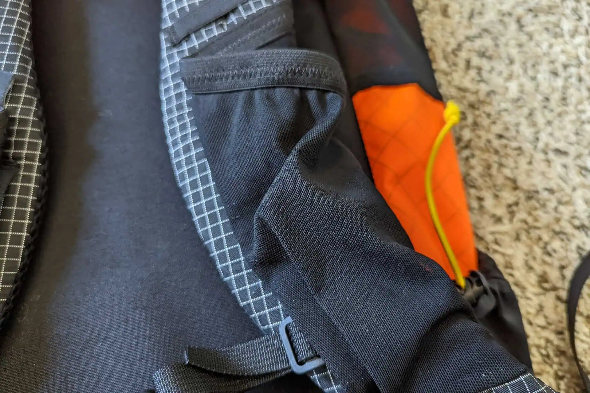 Close-up of the Atom Packs Pulse backpack featuring a black design with gray grid patterns and stitching. An orange section with a yellow drawstring adds flair, while the fabric textures are clearly visible, showcasing premium materials and meticulous craftsmanship.