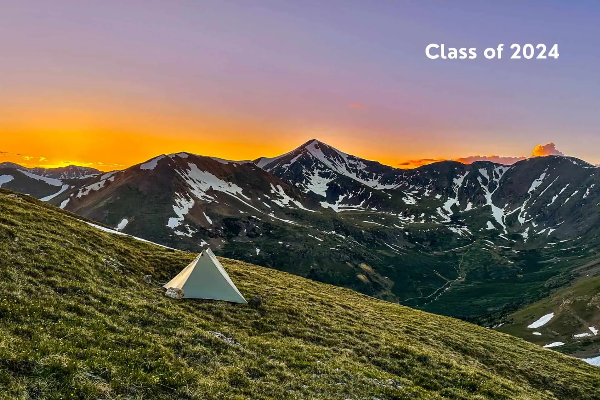A tent rests on a grassy hillside, framed by a breathtaking mountain range. The vivid sunset sky casts hues over snow-dotted peaks. Class of 2024 graces the top right corner, capturing the essence of adventure—your ultimate CDT Gear Guide 2024 companion awaits.