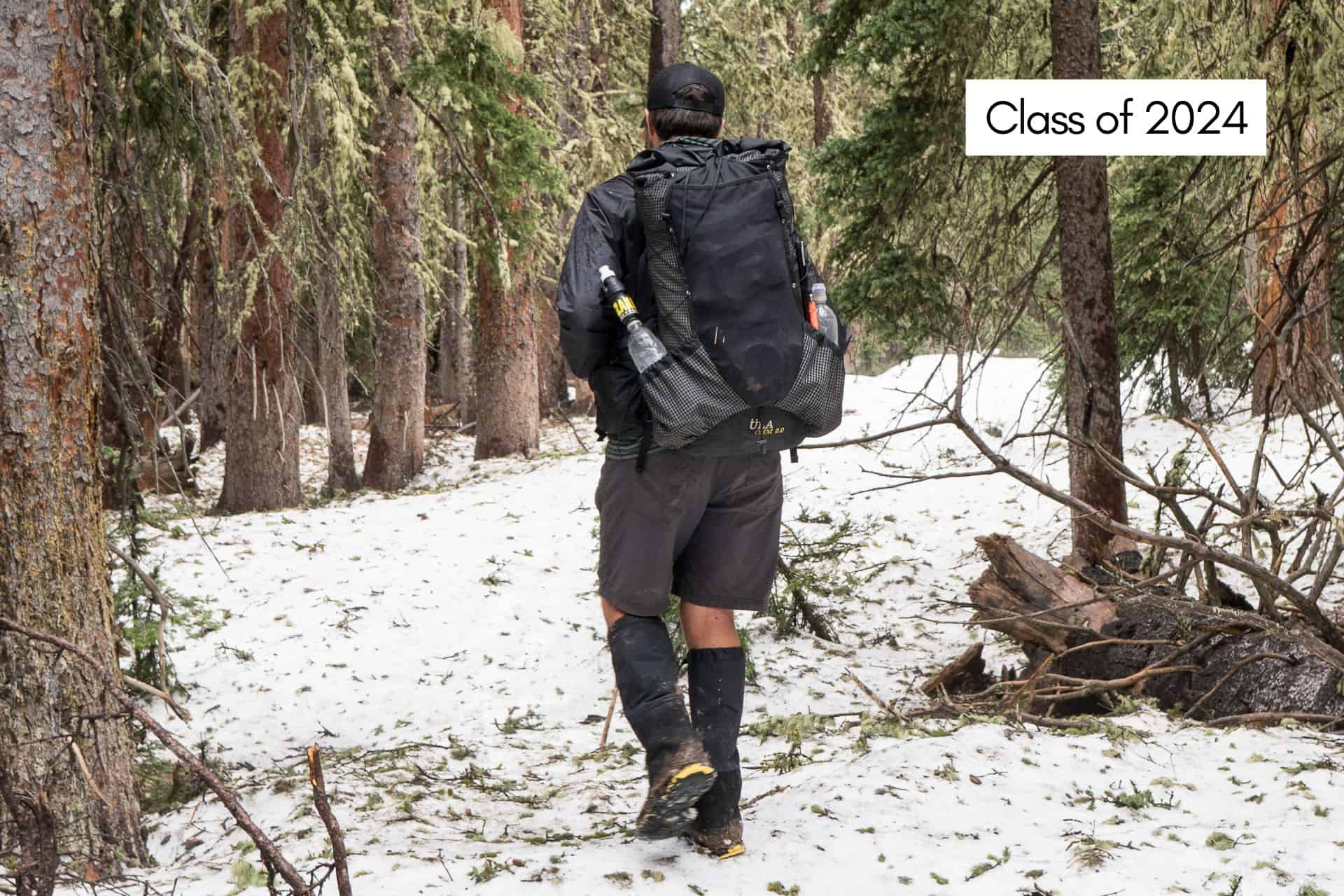 A person with a large backpack navigates the snowy forest trail, donning a cap, black shorts, and gaiters. As they trek on what could be next years Continental Divide Trail journey, text in the image reads Class of 2024.