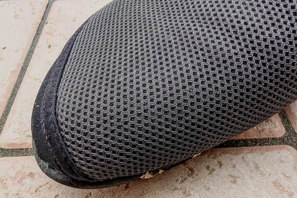 Close-up of a black mesh sneaker toe, branded as BERT Shoes, on a tiled surface. The detailed texture of the shoe material is visible, along with some debris on the shoes edge. The ground features light-colored, patterned tiles.