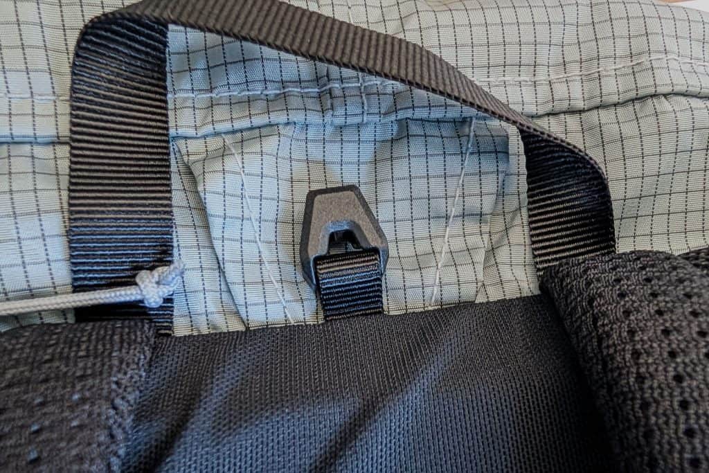 Close-up of the Gossamer Gear Grit 28L Fastpack showcasing its gray grid-patterned fabric. Black straps and a plastic hook highlight the construction details and texture, while a knotted cord peeks out from the side, reflecting its rugged design.