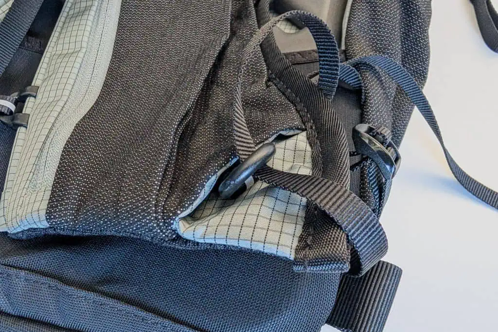 Close-up of the Gossamer Gear Grit 28L Fastpack in black and gray, showcasing its detailed stitching and adjustable straps with buckles. The fabric features a grid pattern, and the pack is laid on a flat surface.
