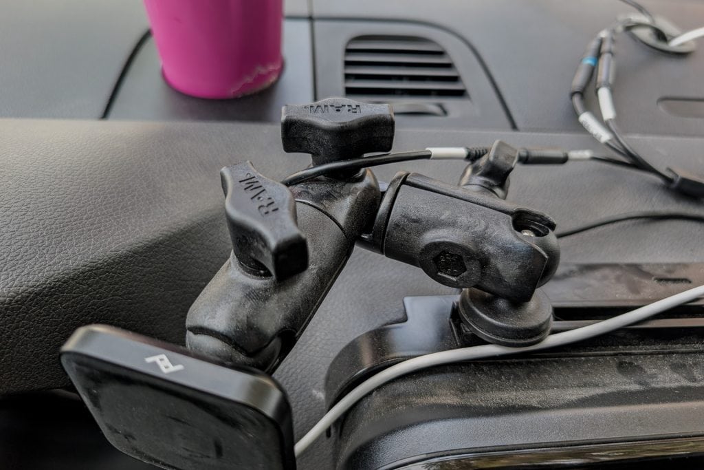 A close-up of a black adjustable phone or camera mount attached to a car dashboard, with a pink travel mug and some cables in the background hints at Wireless Android Auto/Apple CarPlay setup in a 2023 Mercedes Sprinter Van.