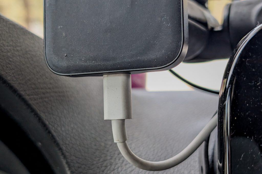 A close-up of a smartphone connected to a charging cable, with part of the phone mount and car dashboard visible in the background, showcases Wireless Android Auto/Apple CarPlay in a 2023 Mercedes Sprinter Van.