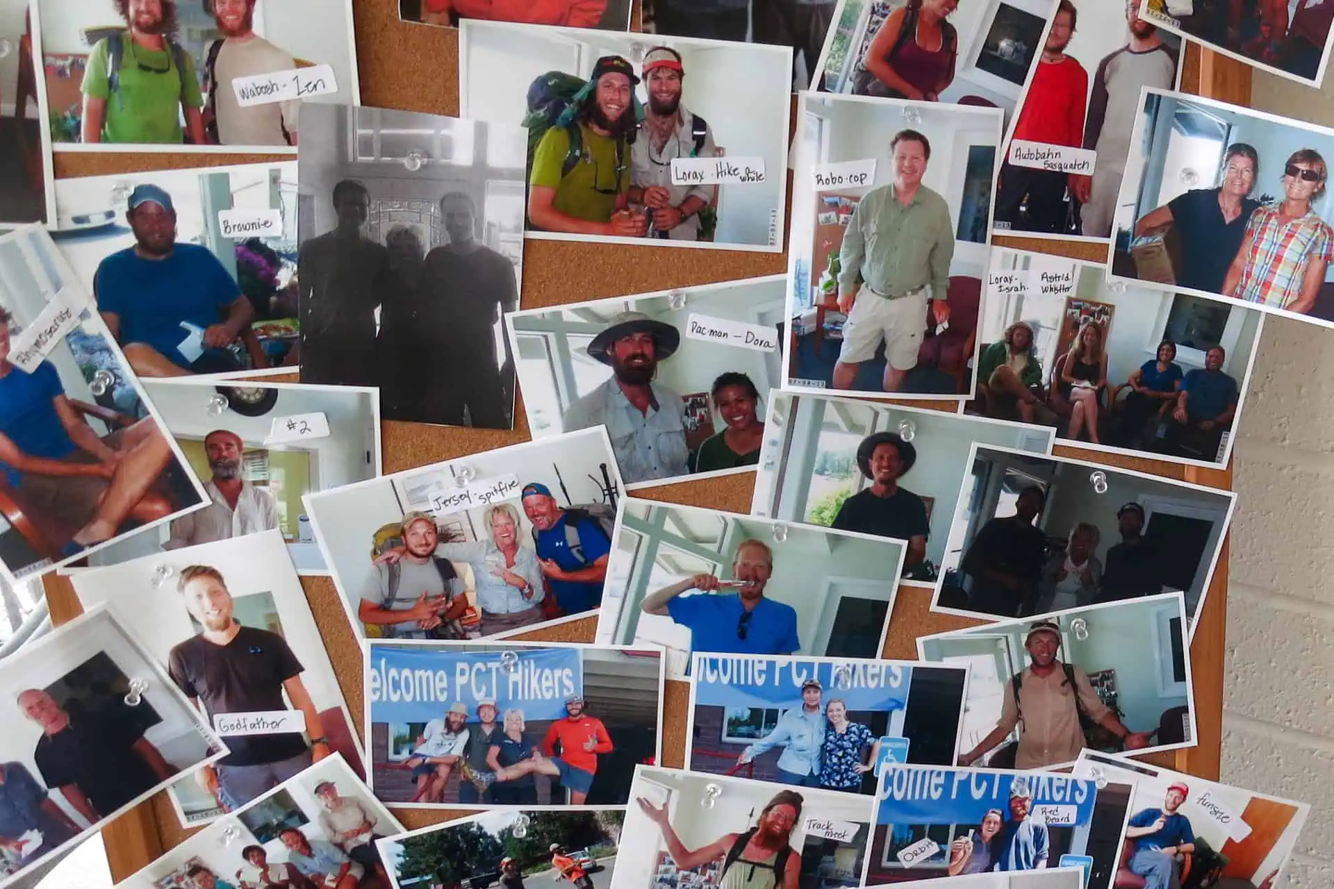 A corkboard covered with photos of various hikers, many smiling and posing with others. Several pictures have handwritten labels or messages, capturing 2024 best PCT moments beneath a Welcome PCT Hikers sign in some images.