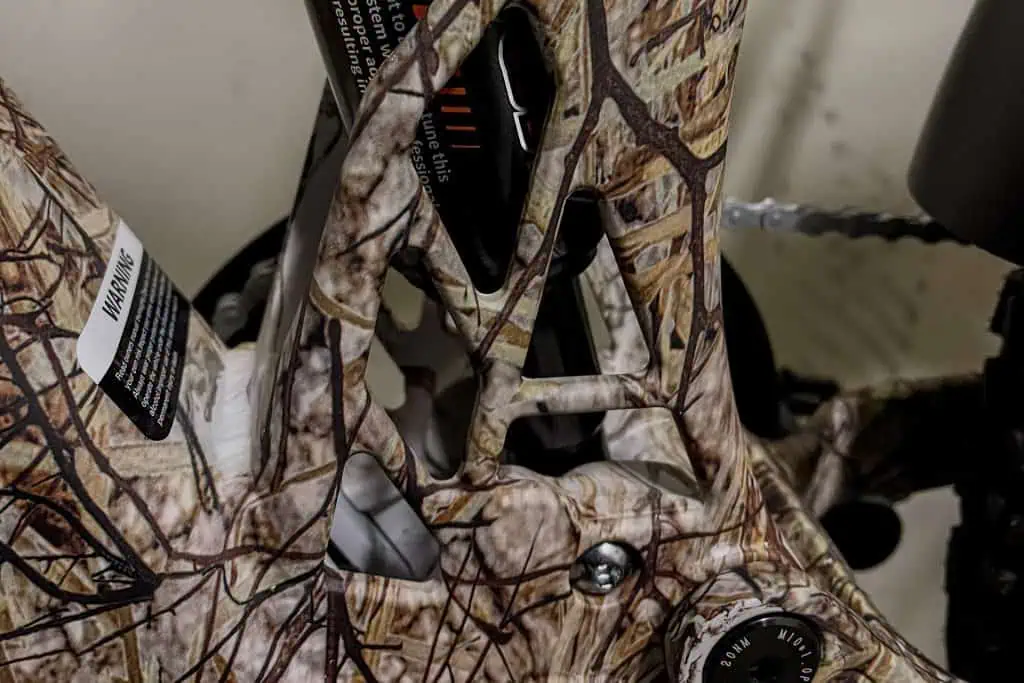 Close-up of a camouflaged PUCKIPUPPY Bulldog electric bike frame, featuring visible warning labels, chain, gears, and a black suspension component within the patterned structure.