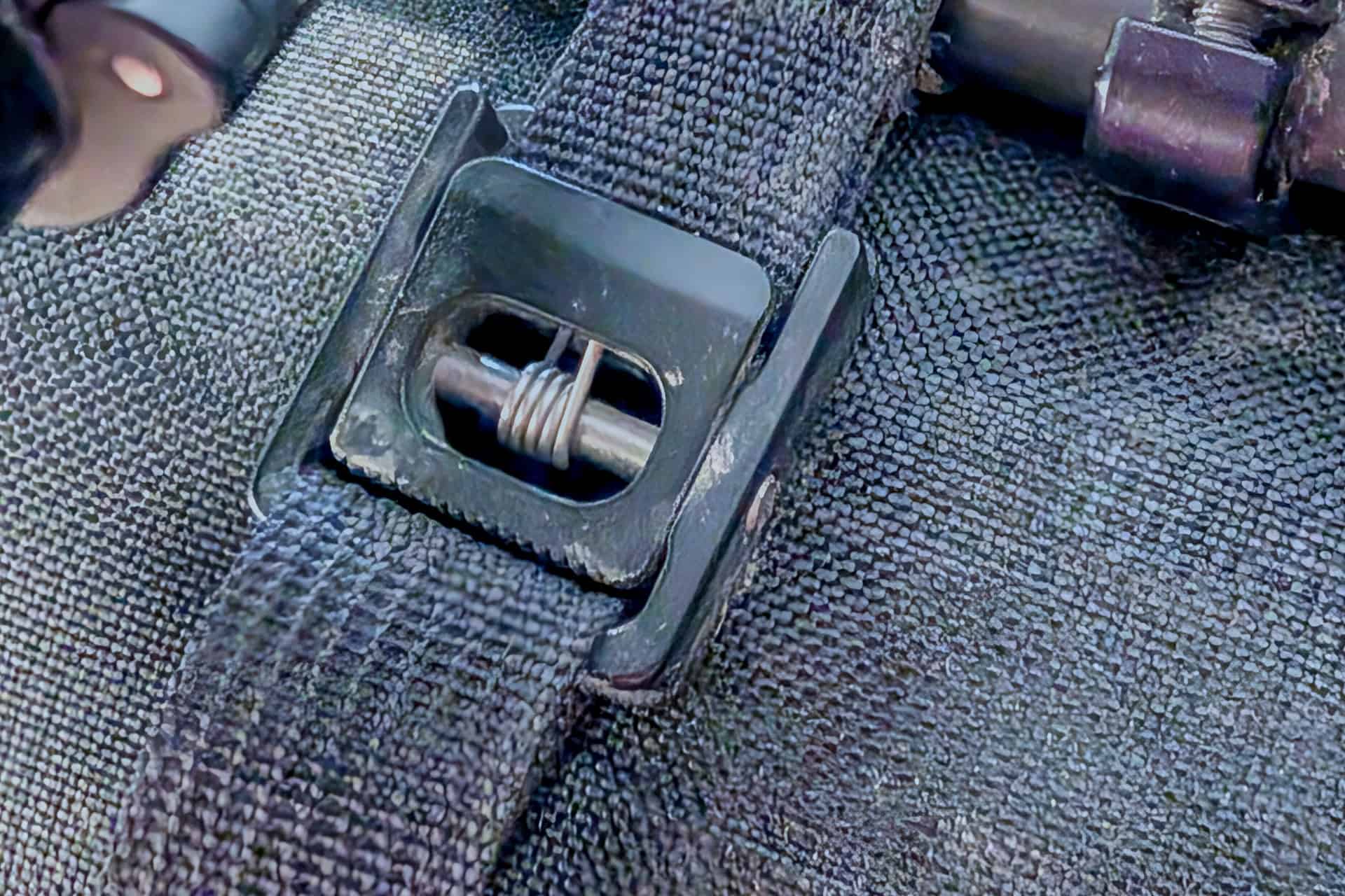 Close-up of a black plastic buckle attached to a woven strap on the Gossamer Gear Grit 28, highlighting the detailed stitching and fastening components against the textured fabric surface.