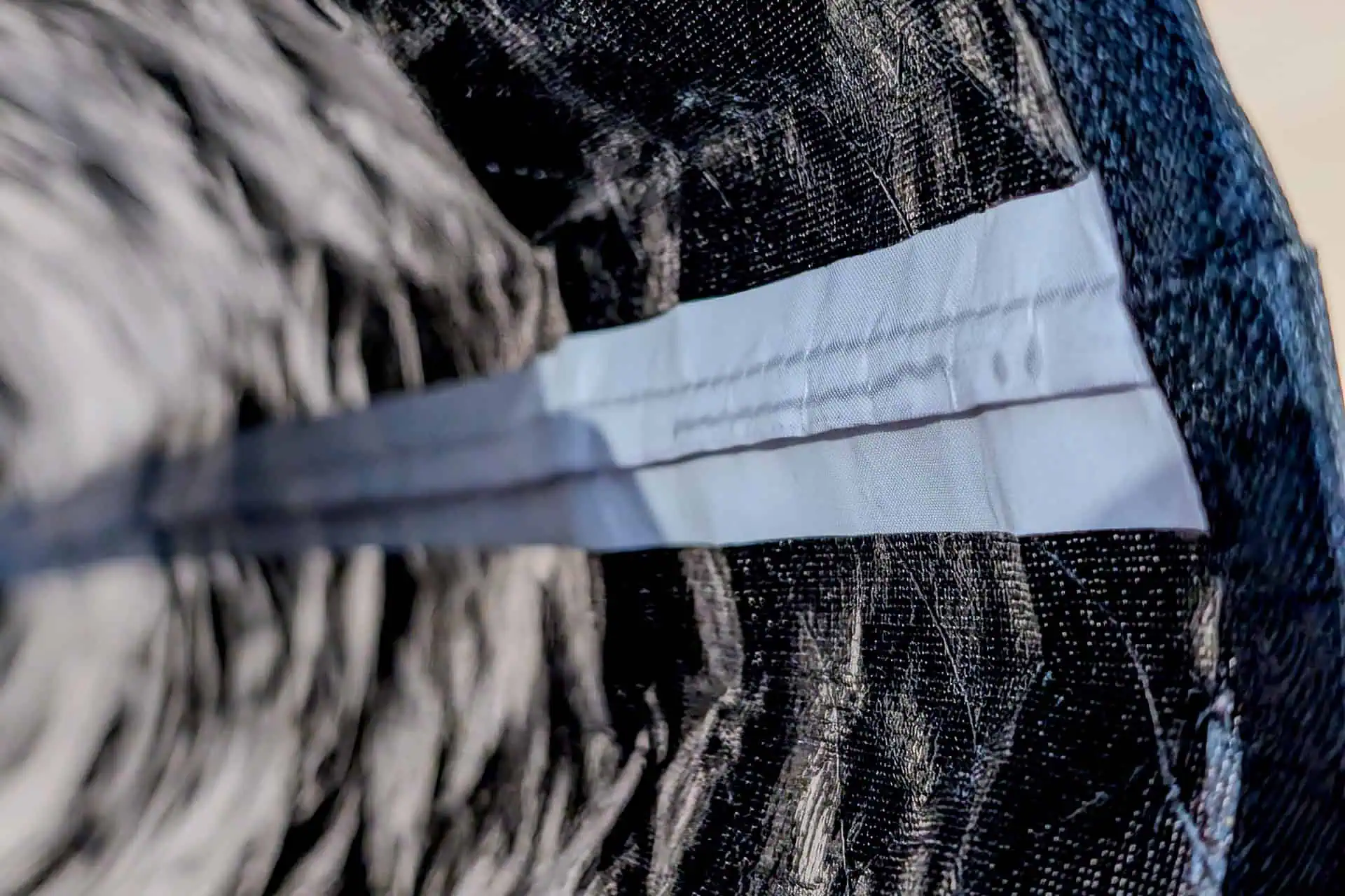 Close-up of a blue medical face mask lying atop crumpled black fabric, its pleated texture and stitched edge in detail—reminiscent of the technical fabrics found on the Gossamer Gear Grit 28.