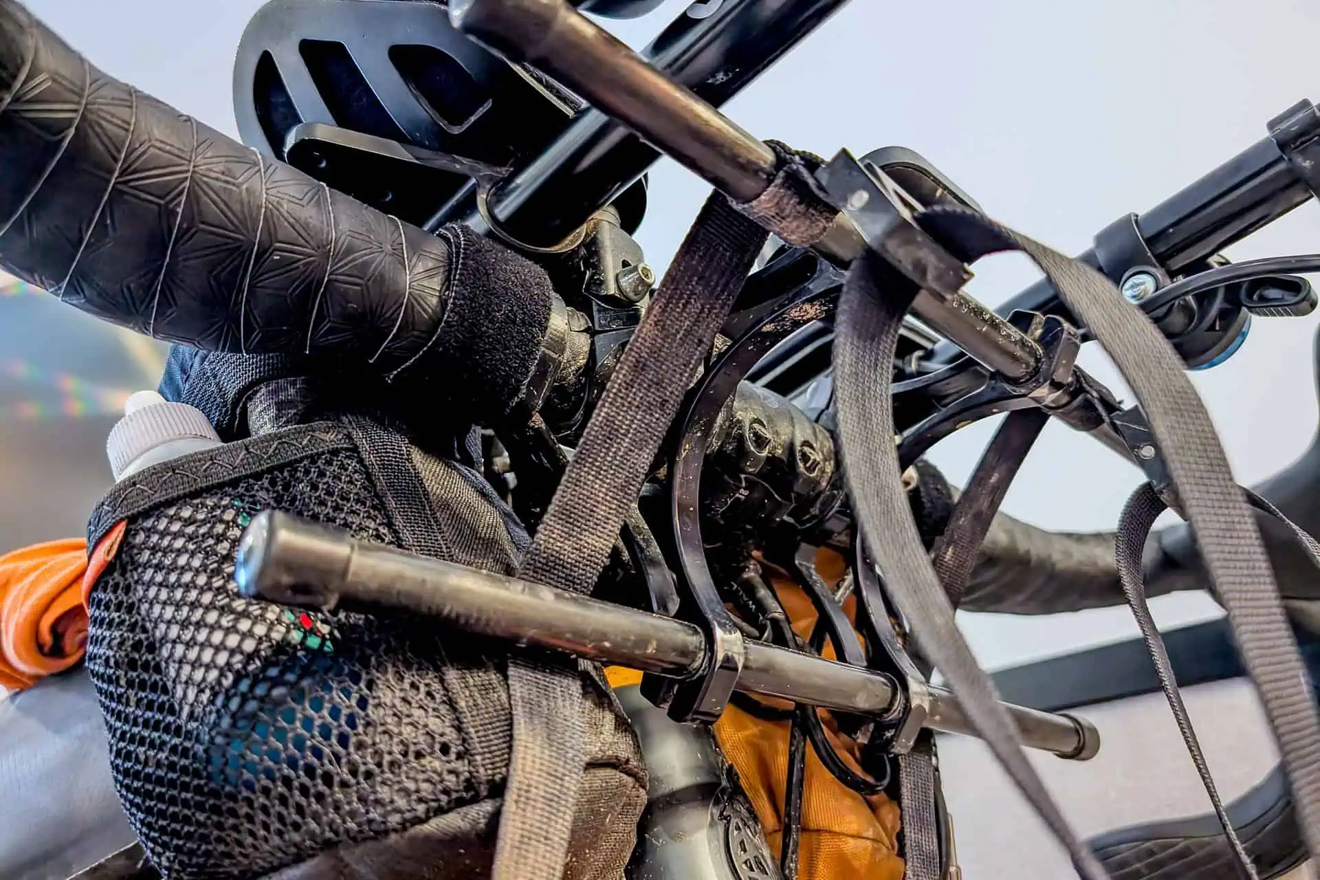 Close-up of a bicycle’s handlebars with attached gear, including a helmet, bags, straps, and a Gossamer Gear Grit 28. The image shows a detailed view of the handlebar accessories and packing setup.
