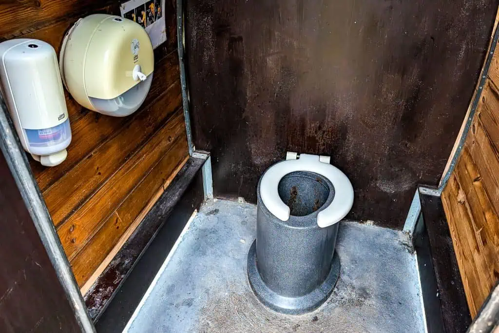 A public restroom with a basic, open-front toilet seat on a cylindrical base, surrounded by wooden and dark metal walls—an amenity often found along the Pyrenees High Route (HRP), featured in many hikers photo galleries.
