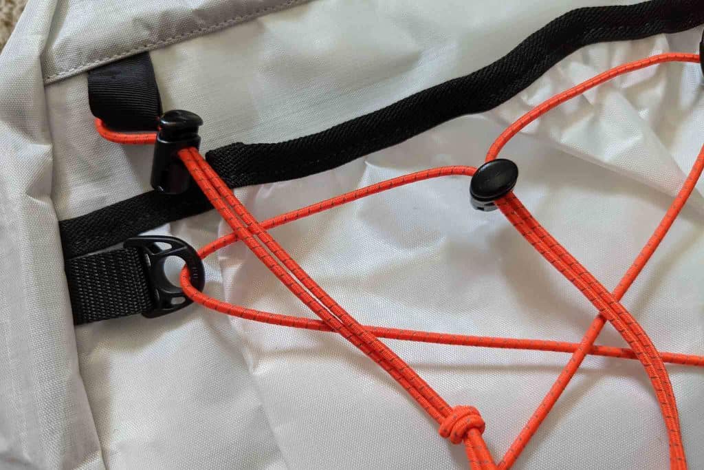 Close-up of orange elastic bungee cords with black plastic clips and sliders attached to a light gray fabric surface, likely part of a Rogue Panda Blue Ridge Handlebar Harness or similar outdoor gear.