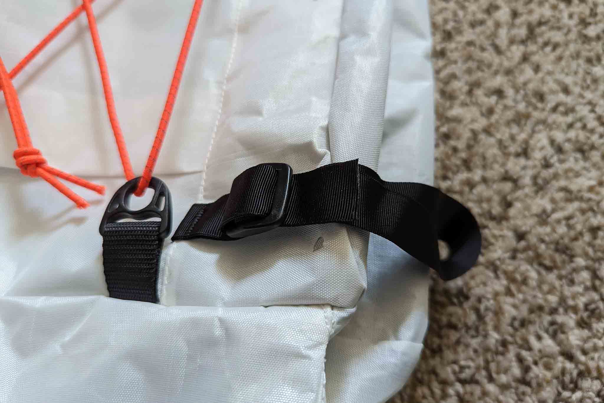 Close-up of a gray fabric bag, possibly used with the Rogue Panda Blue Ridge Handlebar Harness, featuring an orange cord through a plastic loop, a black strap with an adjustable buckle, and beige carpet in the background.